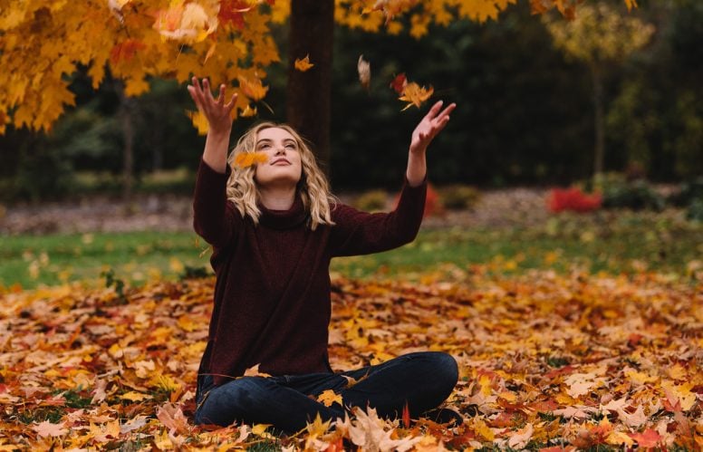 Happy female student sitting and playing in leaves
