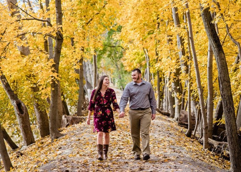 Engaged couple walking and laughing through leaves